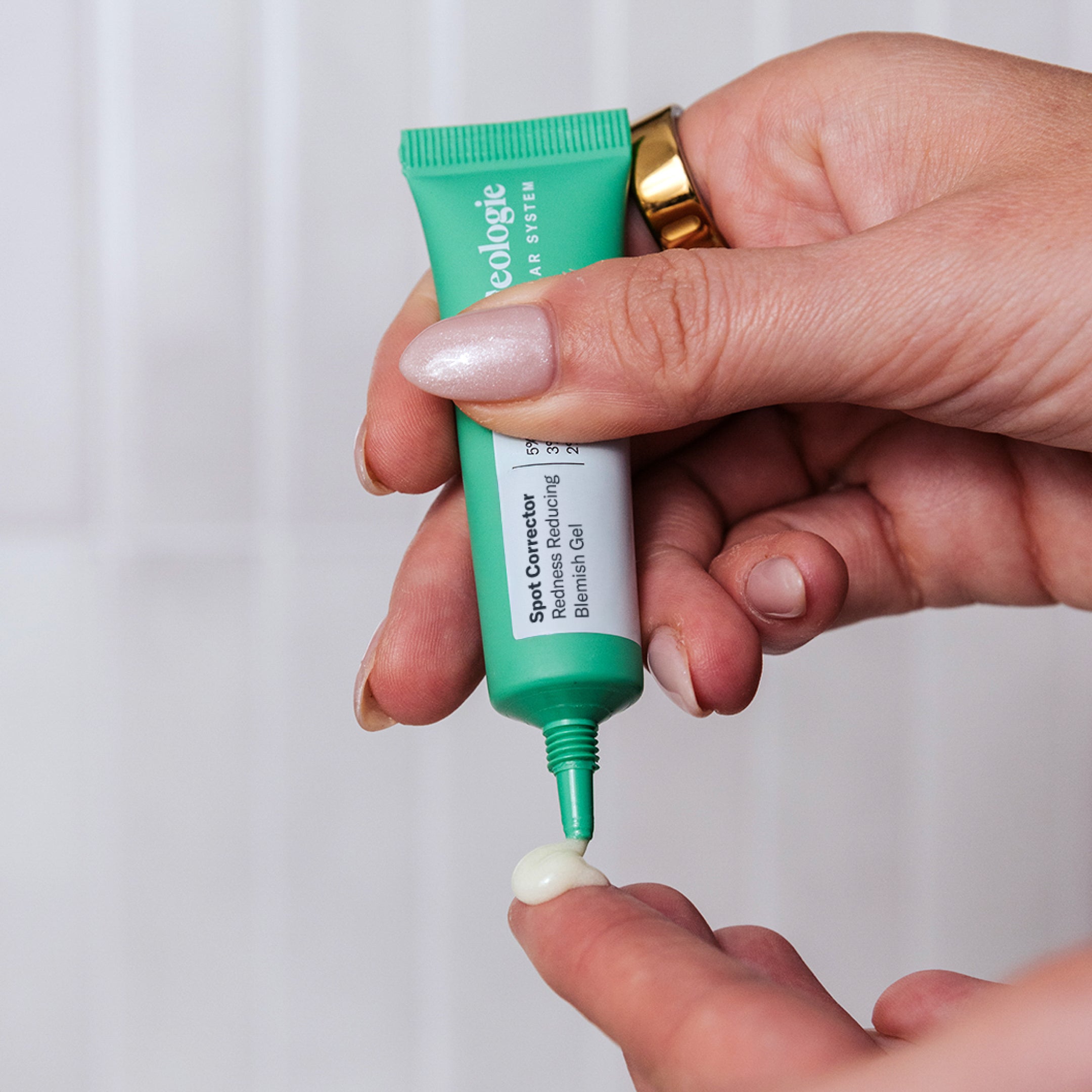 A person squeezes a small amount of Geologie's Anti Pimple Pack from a green tube onto their fingertip, ideal for targeted acne treatment, against a light background.