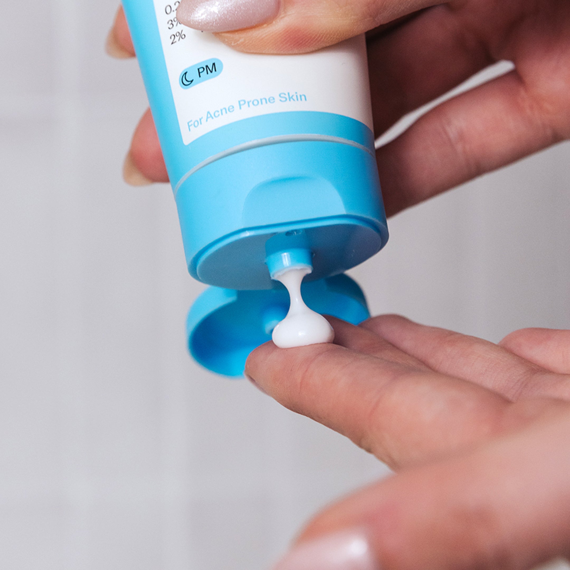 A person dispenses Geologie Skin Repair Moisturizer from a blue and white tube onto their finger, applying this gentle, hyaluronic acid-infused cream for acne treatment.