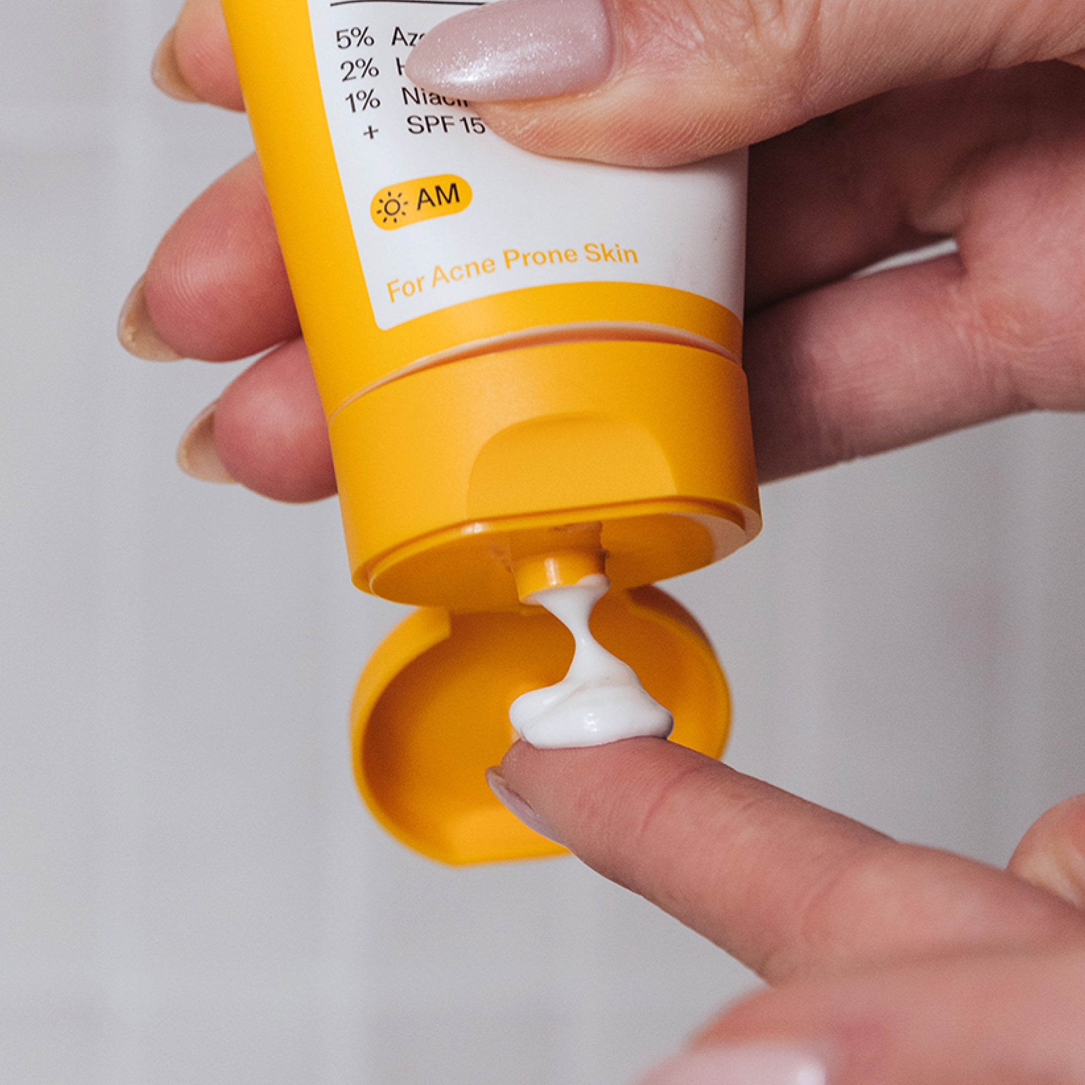 A hand dispenses white cream from a yellow tube labeled “Geologie Clear Skin Face Cream” for acne-prone skin with azelaic acid onto a fingertip.