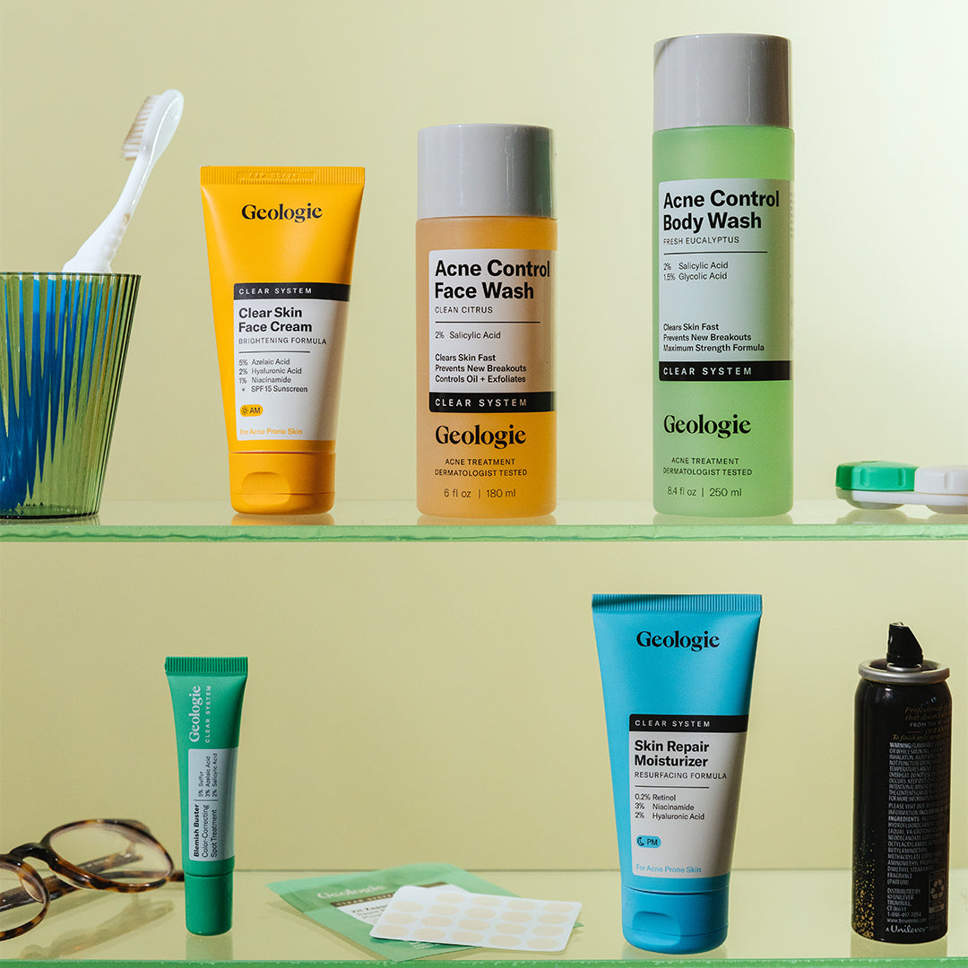 The Geologie Clear System Set, a collection of personal care items, sits on the bathroom shelf alongside essentials like a toothbrush, razor, and acne patches.