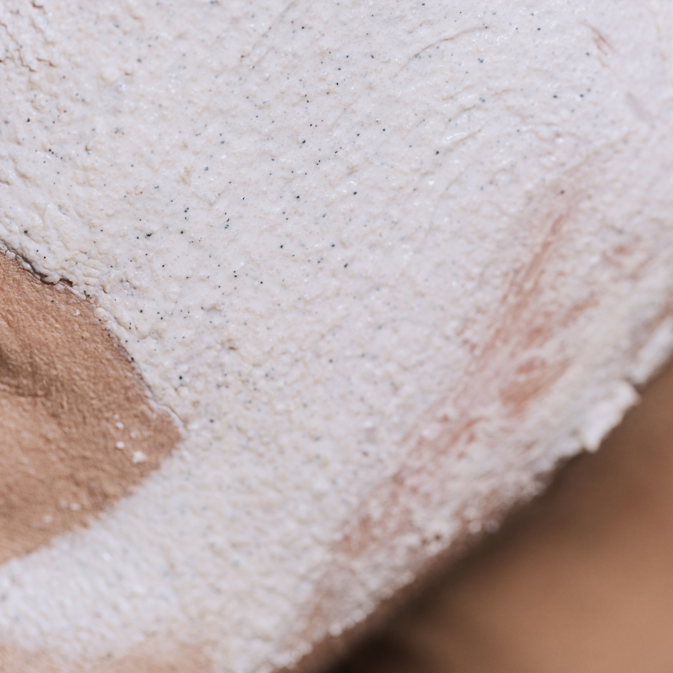 Close-up of a person’s face with a section covered in Geologie's Micro Exfoliator & 3 Minute Clay Mask, highlighting a clean area where the mask has been removed, perfect for a spa day.