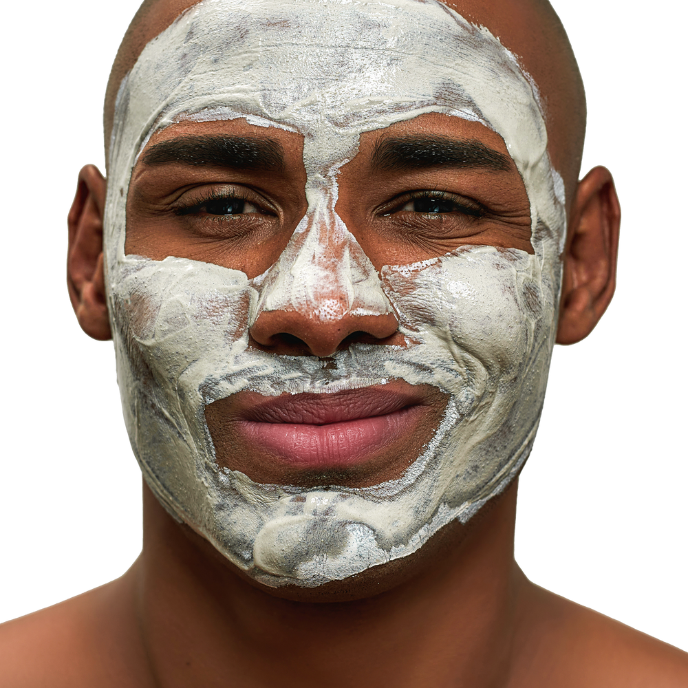 A man with a facial mask applied, smiling slightly against Geologie's Self Care Gift Set, a power-packed bundle of head to toe care against a black background.