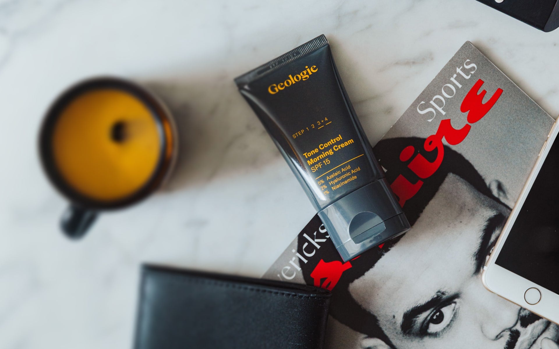Geologic time-activated shaving cream tube on a marble surface with a magazine and mug.