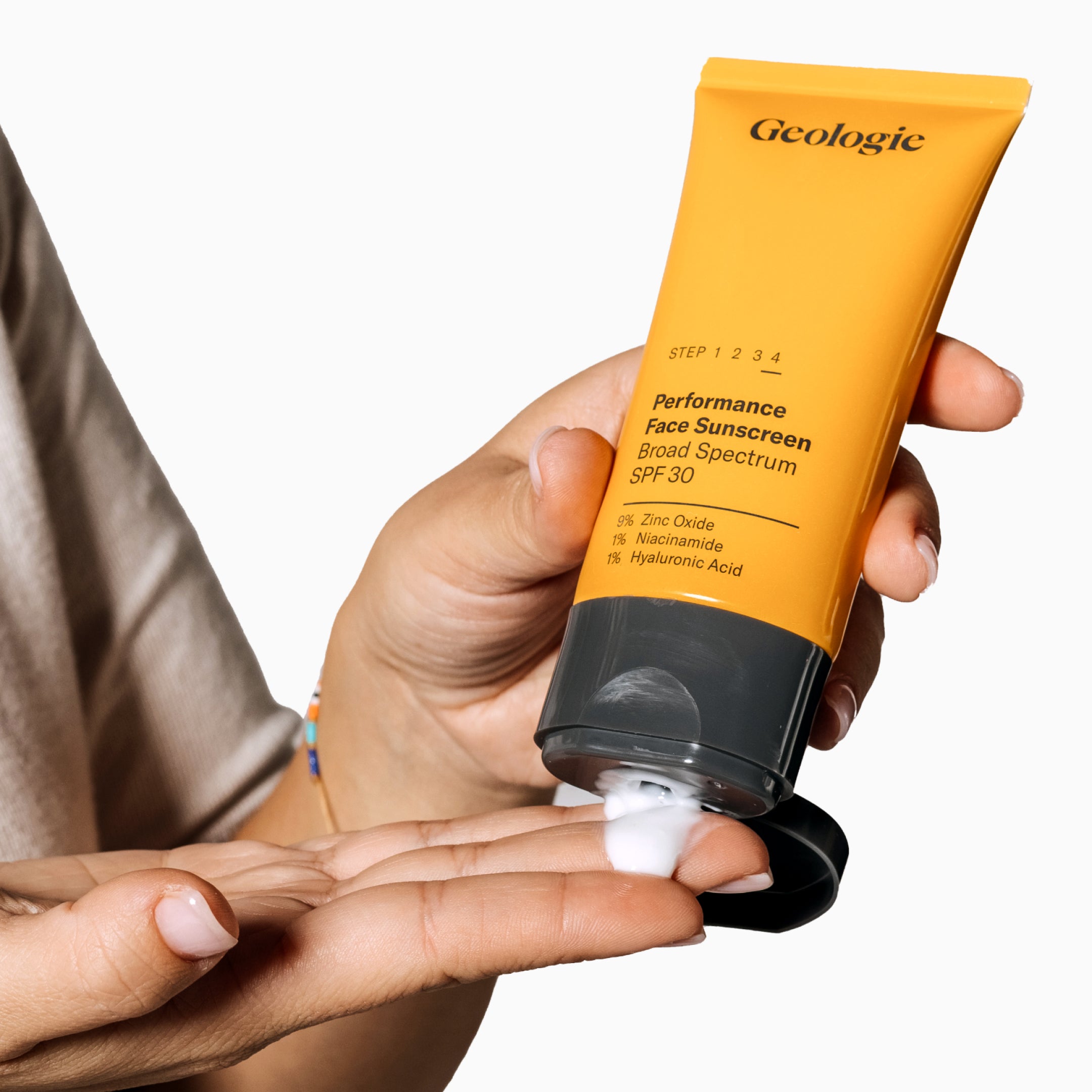Hand squeezing out Sun Protection Essentials sunscreen from a Geologie orange tube.