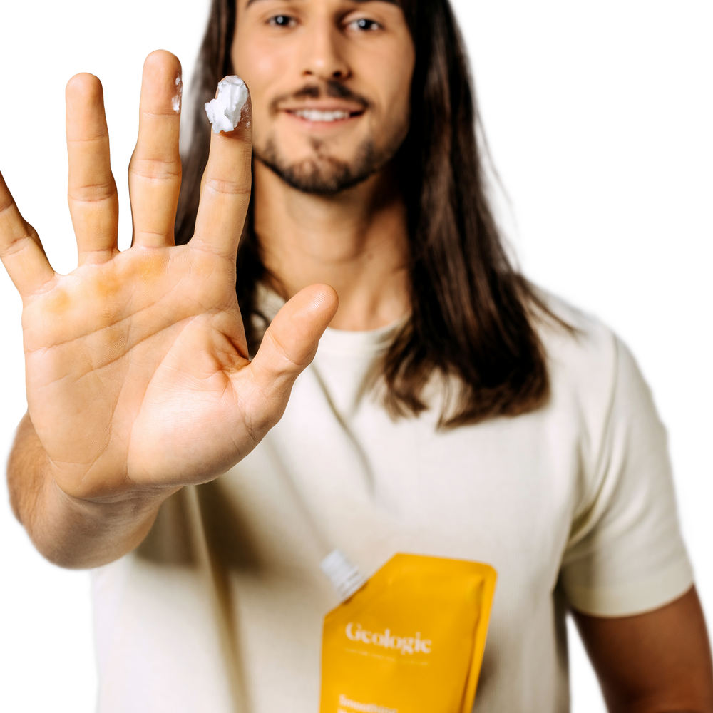 Man with long hair holding a carton and showing Geologie Anti-Dandruff Haircare Set cream on his hand.