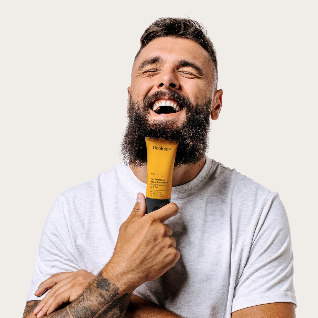 Man with a full beard laughing and holding a yellow tube of Geologie Dark Under Eye Duo.
