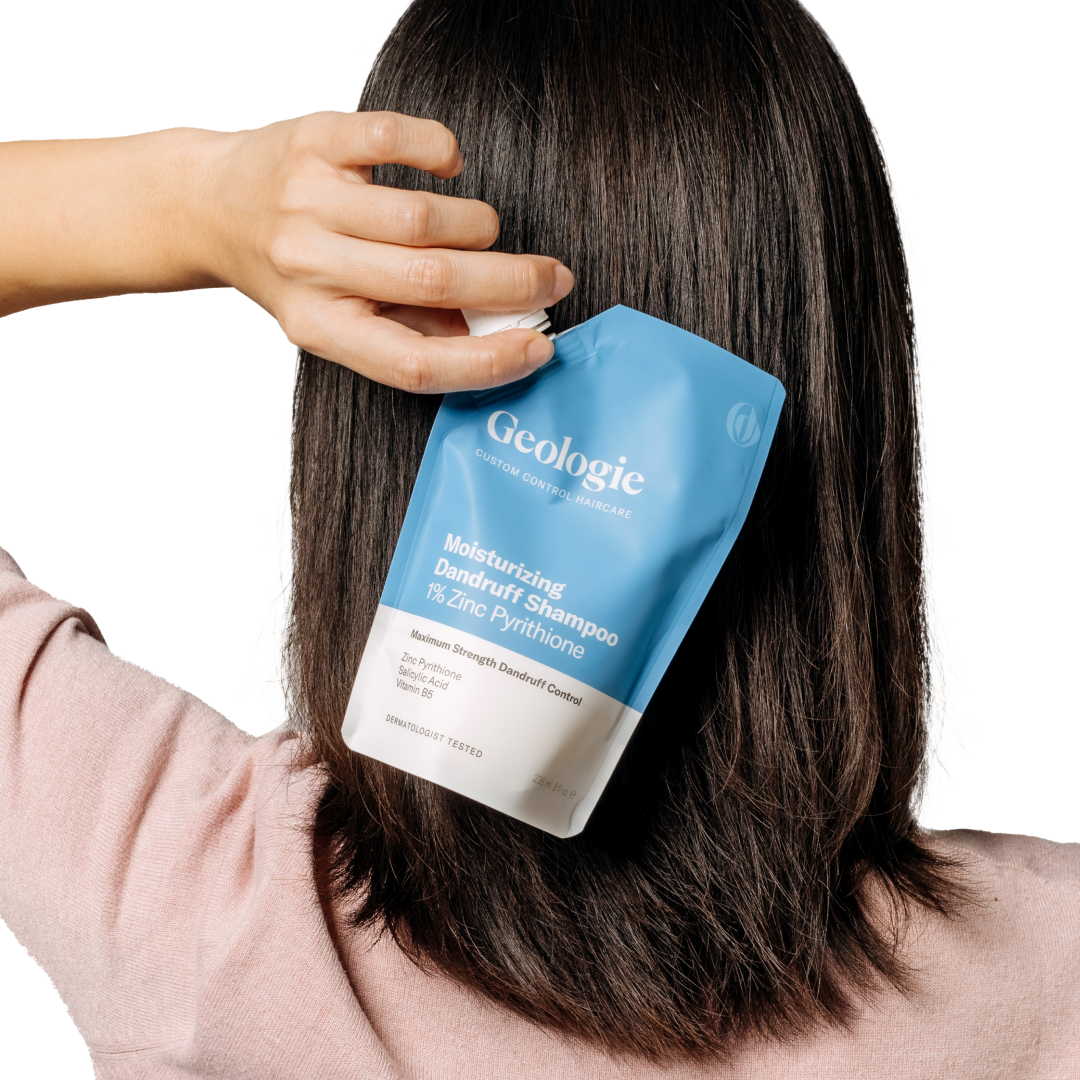 A person holding a Geologie Anti-Dandruff Haircare Set packet near their hair, designed to reduce dandruff.