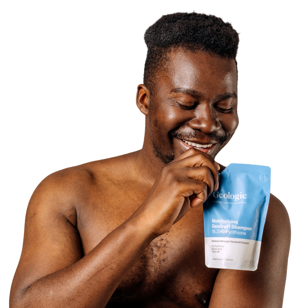 A cheerful man holding a bag of Geologie's Dandruff Shampoo + Conditioner Bundle that prevents dandruff.